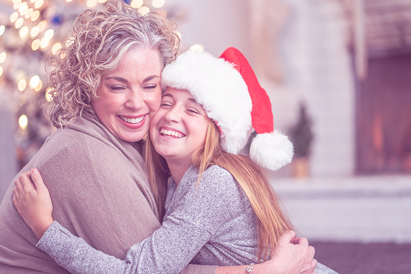 woman embracing a child with a santa hat on during the holidays