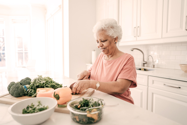 gray haired black woman cutting vegetables in the kitchen