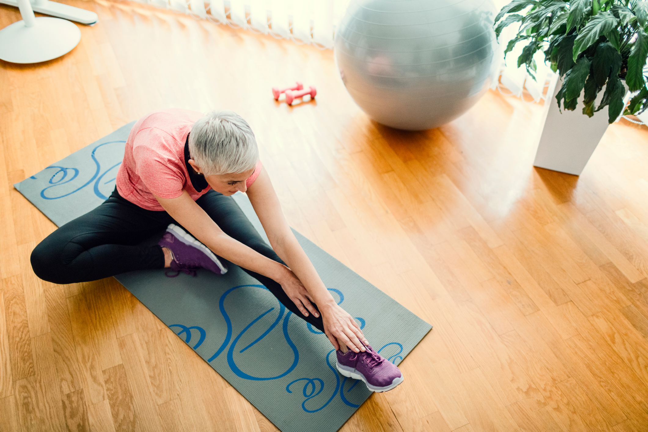 gray-haired lady stretching on a yoga mat at home