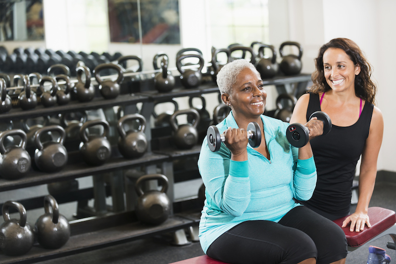 a personal trainer helps a middle age woman lifting weights