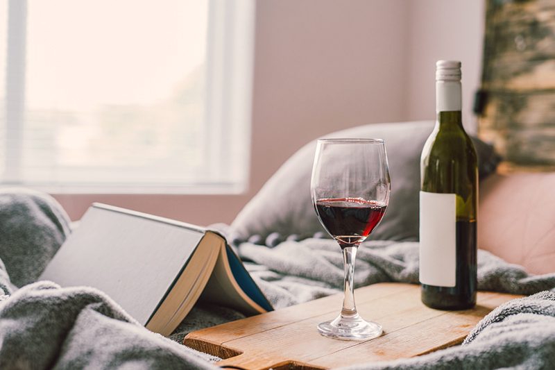 a glass of red wine and a book on the bed at home