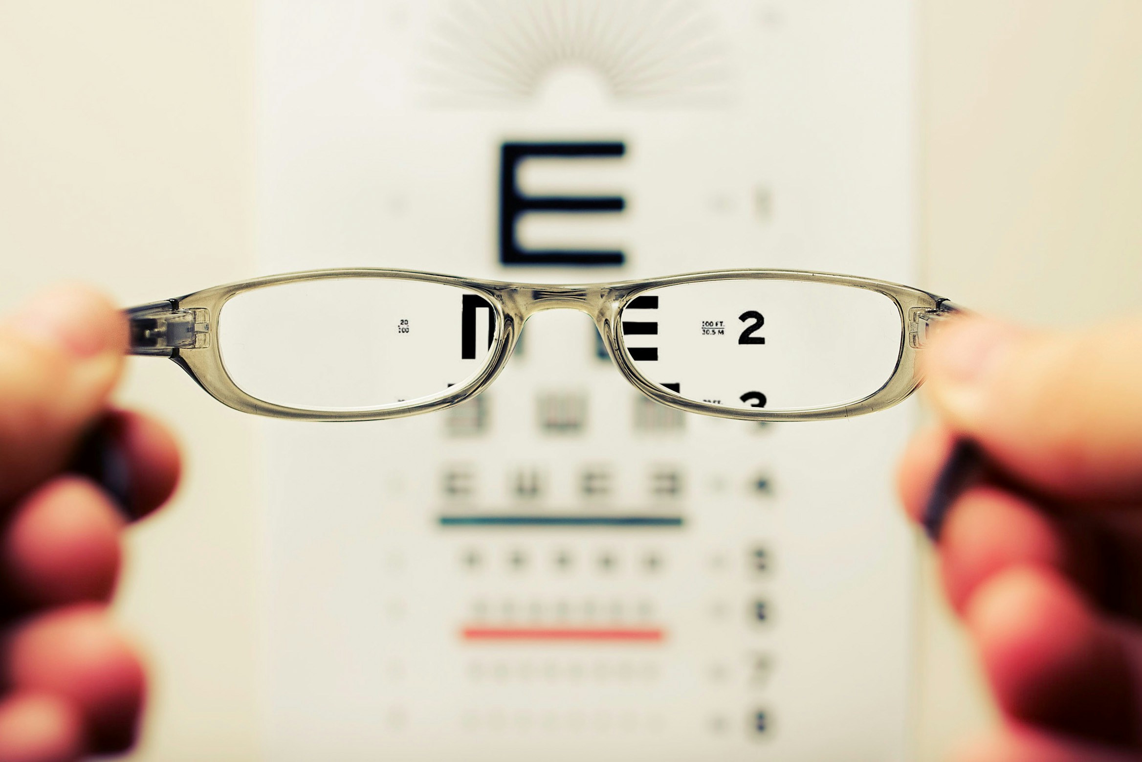 Image of someone holding eye glasses infront of eye test chart