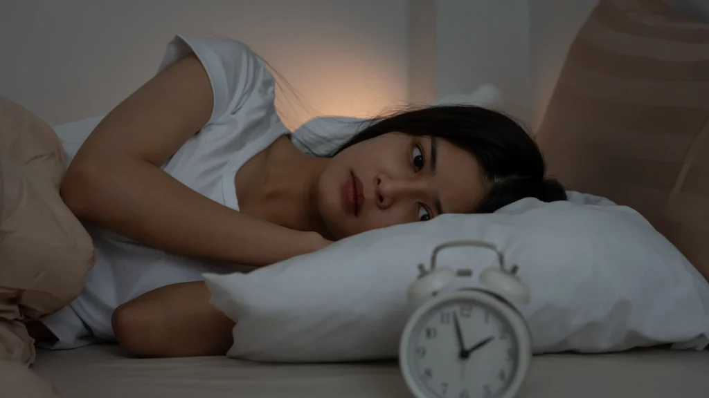 A woman in bed, unable to sleep, staring at the clock