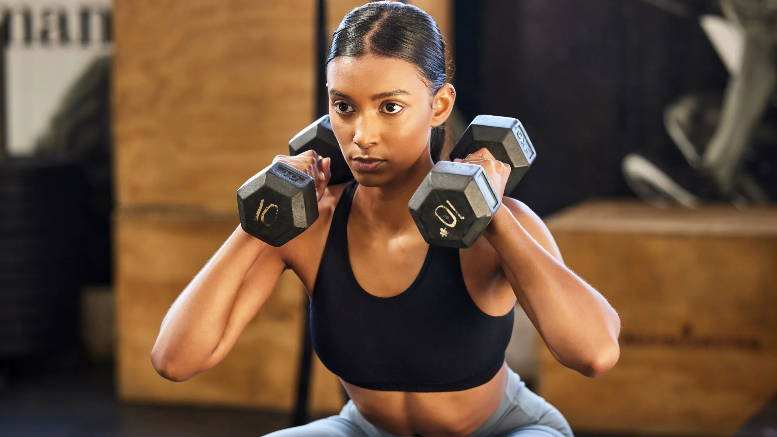 Woman performing a strength-training exercise with dumbbells in a gym.